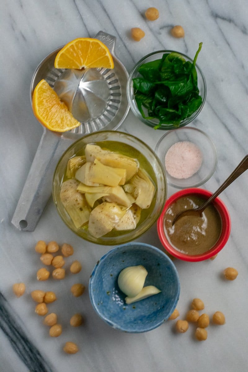 Garlicky spinach artichoke hummus ingredients in small bowls on marble slab