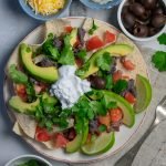 Nachos on beige plate with small bowls nearby
