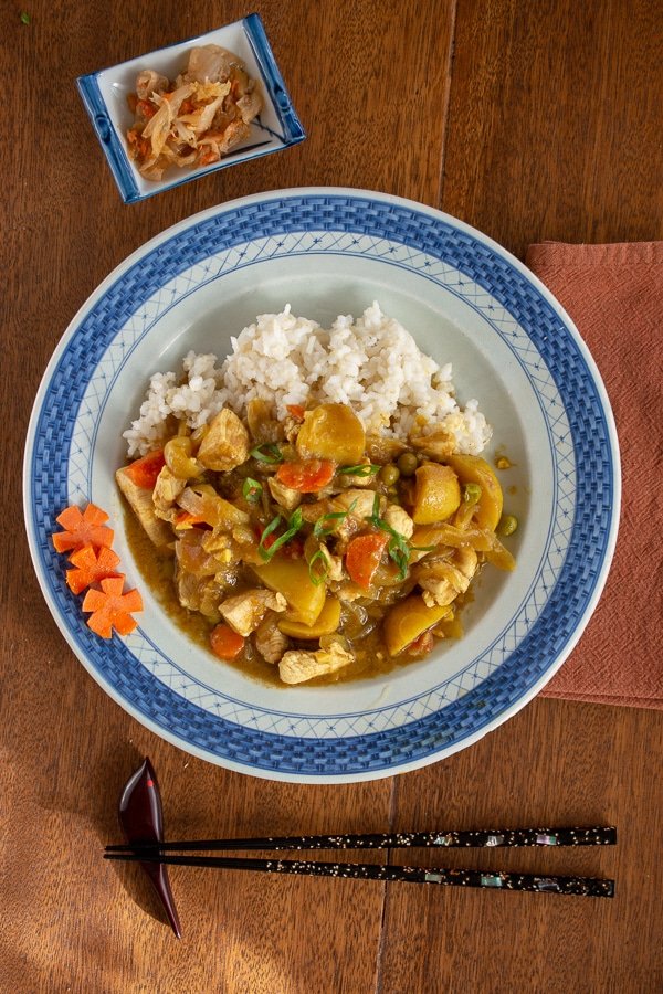 Japanese chicken curry on rice on a blue plate with chopsticks and condiment dish