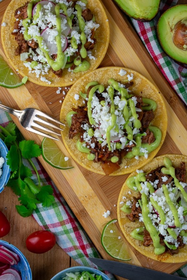 beef barbacoa slider tacos with avocado lime dressing on wood board