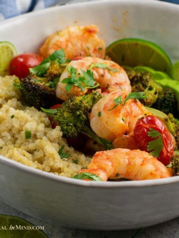 close up of roasted shrimp with broccoli and tomatoes in bowl with quinoa and avocado