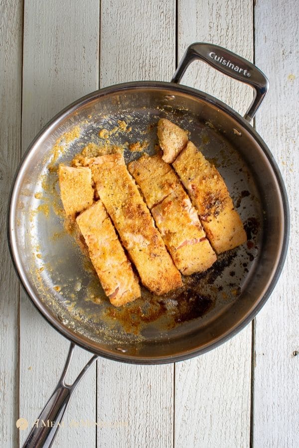 seared salmon fillets with almond flour coating in stainless skillet