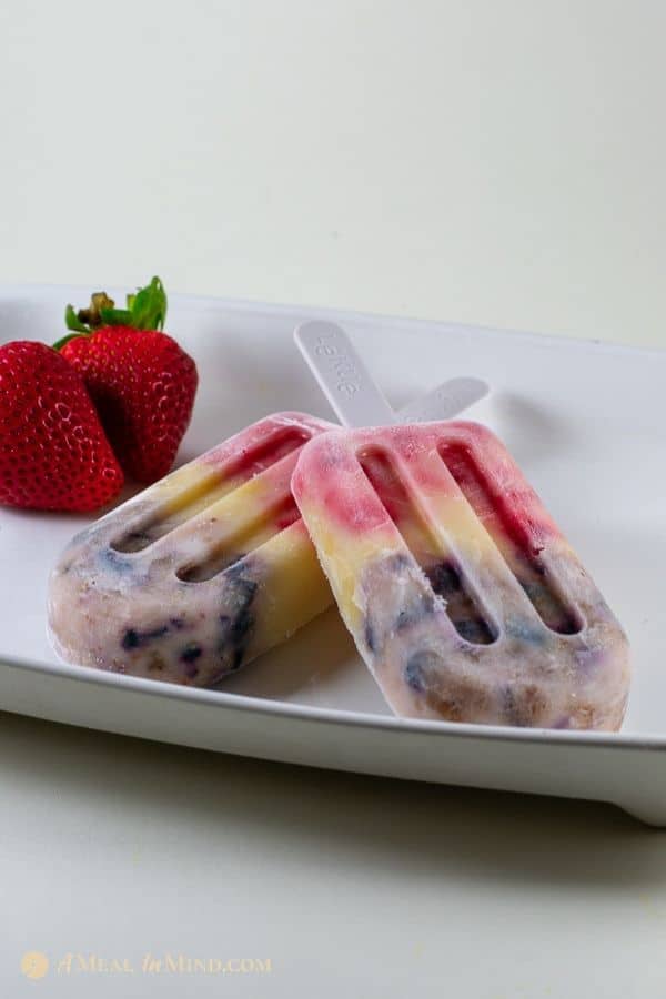 frosty coconut yogurt fruit popsicles with fruit on white tray