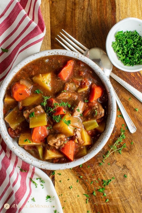 old fashioned oven baked beef stew in white bowl with striped cloth