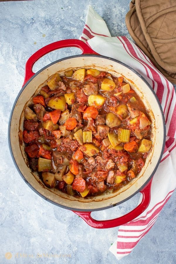 old fashioned oven baked beef stew in dutch oven with striped cloth