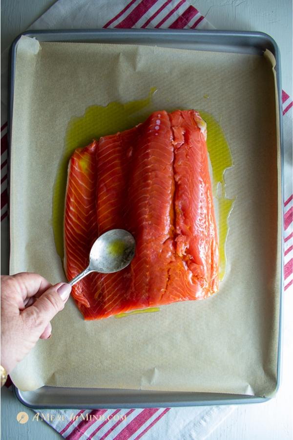 garlic herb salmon baked in parchment side spreading olive oil on fillet in pan