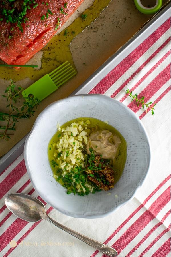 garlic herb salmon baked in parchment ingredients for sauce in white bowl