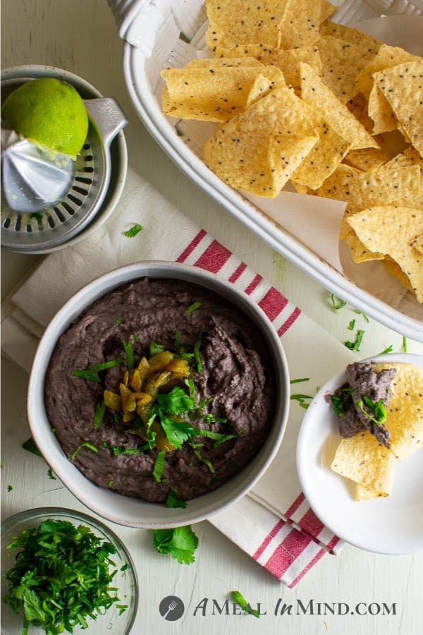 cheese green chile black bean dip in white bowl with corn chips