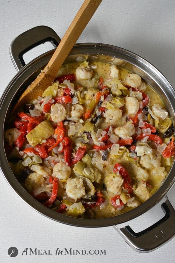 shrimp pasta with olives and artichoke hearts in skillet with wooden spoon