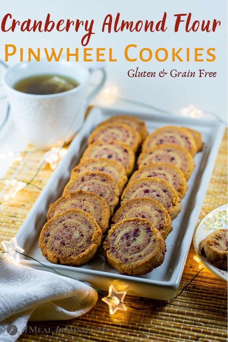 pinterest image of cranberry almond-flour pinwheel cookies on a white platter with a cup of tea