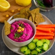 Beet Artichoke Hummus in small bowl on plate with vegetables