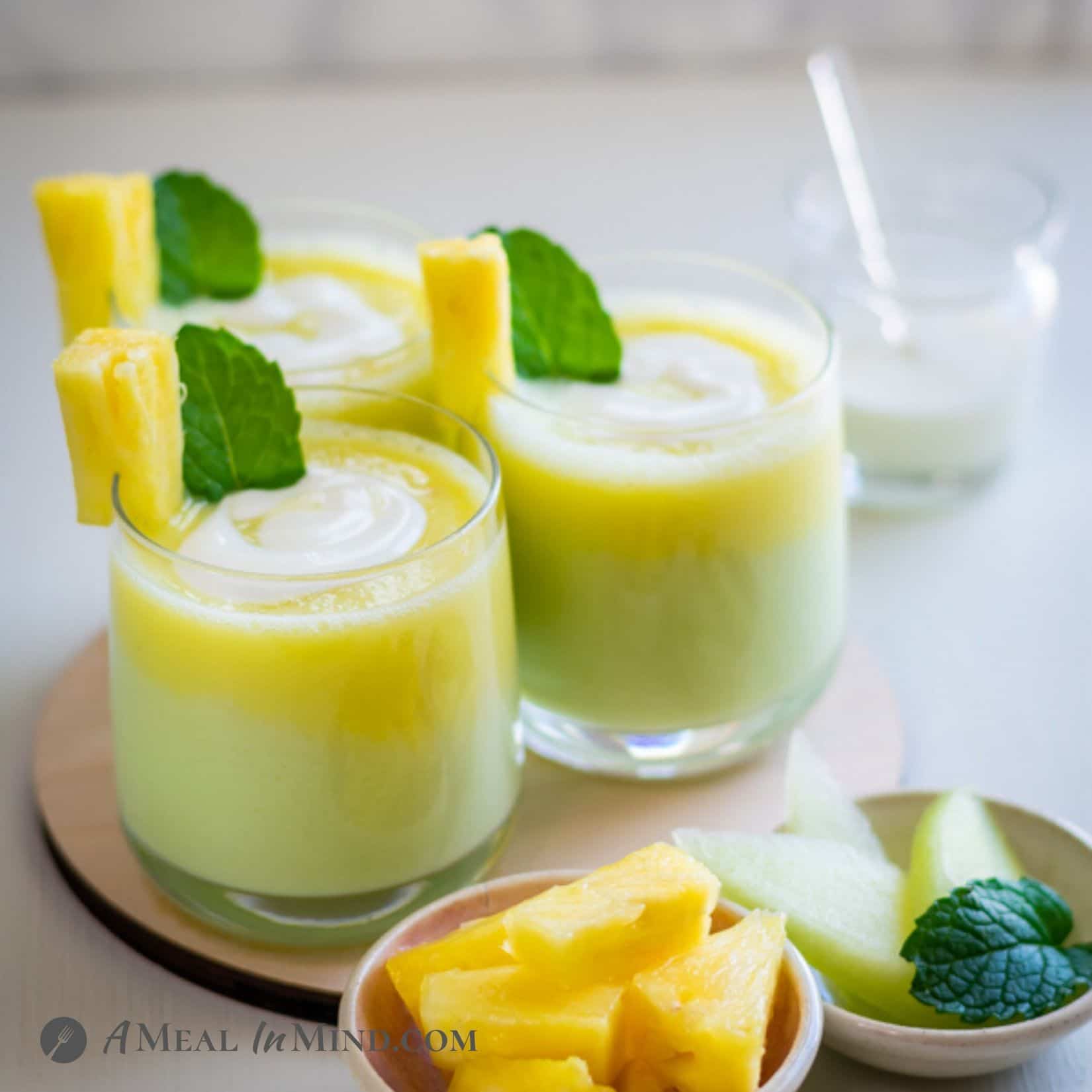 Layered Pineapple-Honeydew Lassi in three clear glasses with pineapple garnish