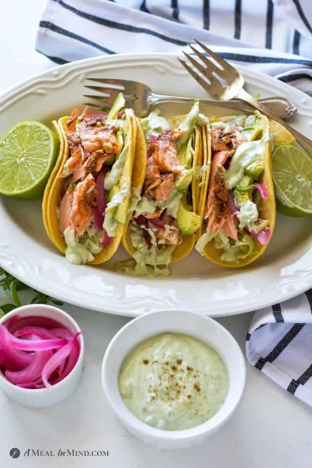Parchment-Roasted Salmon Tacos with Yogurt-Avocado Crema on white platter