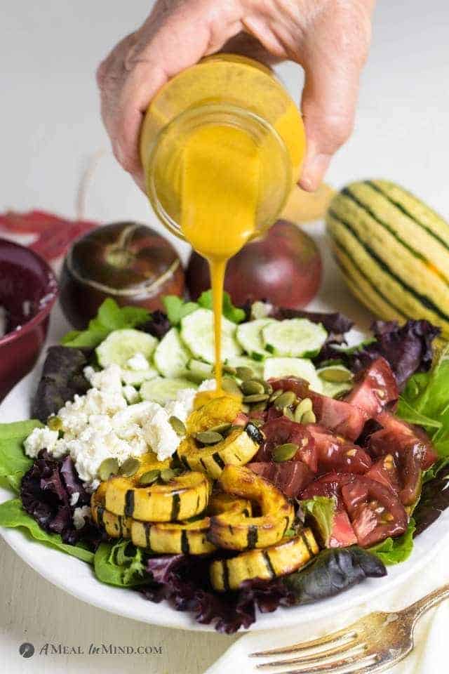 pumpkin-colored salad dressing being poured onto a bowl of salad