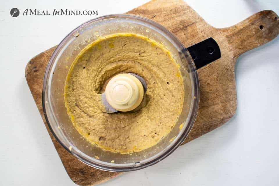 Eggplant Hummus in food processor on wooden board