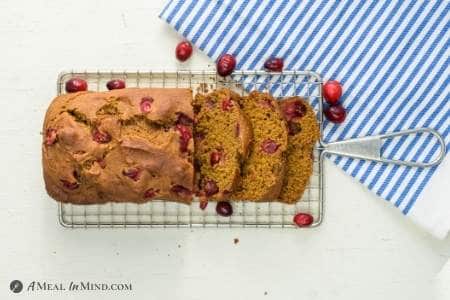 Cranberry pumpkin bread partly sliced on wire rack