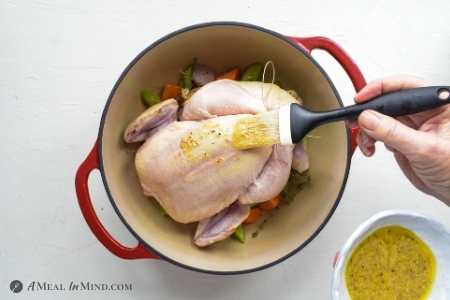 chicken being brushed with lemon-mustard glaze in dutch oven