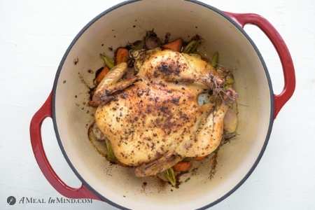 roasted chicken in dutch oven on a bed of vegetables
