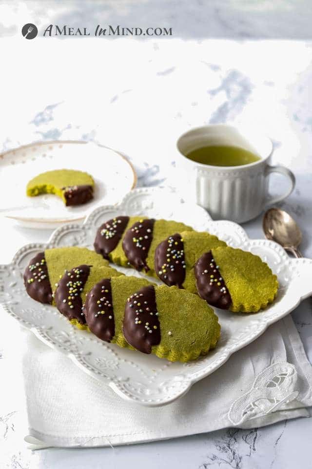 dark chocolate-dipped matcha cookies on plate with a cup of tea