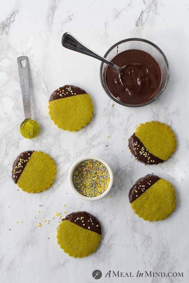 chocolate dipped paleo matcha cookies with matcha, chocolate and sprinkles on counter