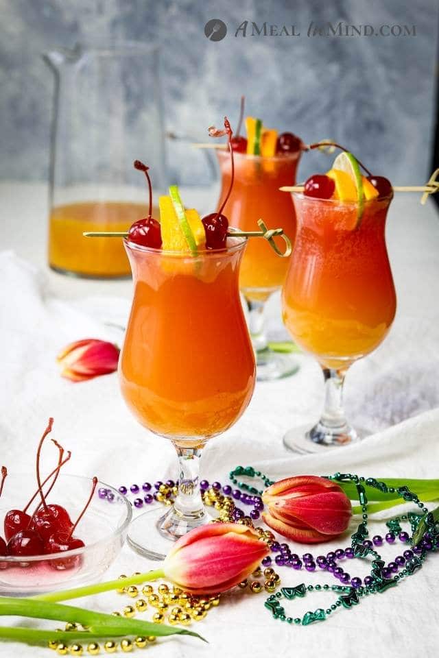 three hurricane mocktails with garnishes and mardi gras beads on white cloth